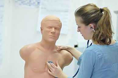 Studentin hört an einer Simulationspuppe mit den Stethoskop Herztöne ab.