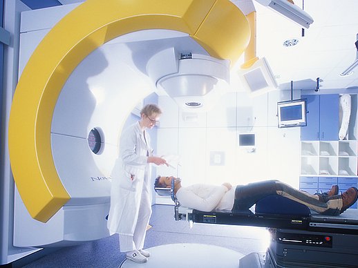 Ärztin steht hinter Patient und spricht mit ihm, umgeben von einem großen runden weiß-gelben Gerät.