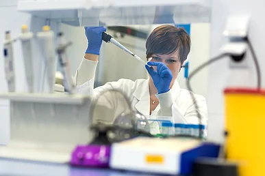 Immunologisches Labor der Medizinischen Klinik 3 – Rheumatologie und Immunologie Labormitarbeiterin in weißem Kittel und mit blauen Laborhandschuhen gibt mit einer Pipette eine dunkle Flüssigkeit in ein Reaktionsgefäß.