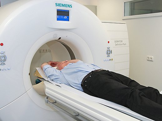 Älterer Herr fährt mit nach oben gestreckten Armen in ein Siemens-MRT-Gerät.