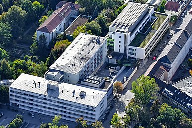 Luftaufnahme von Ost nach West. Diagonal von links nach rechts die drei Hauptgebäude der Kinder- und Jugendklinik. Parallel dazu links das historische im Schlossgarten gelegene Gebäude des Virologischen Instituts.