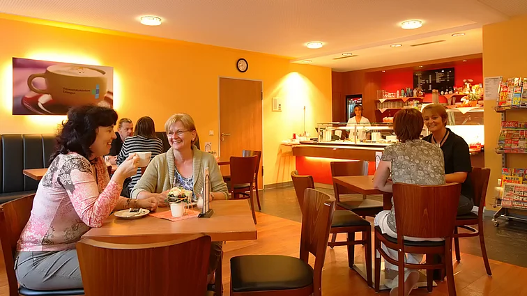 Einige unterhalten sich entspannt bei Kaffee und Kuchen in der in warmen Orangetönen gehaltenen Cafeteria. 