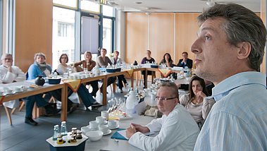 Blick von vorne auf einen Konferenzraum voller Personen die konzentriert nach vorne blicken.