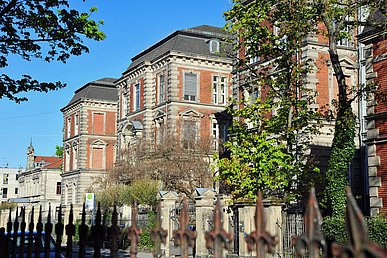 Blick auf das historische Gebäude der Strahlenklinik im Stil der Gründerzeit mit roter Klinkerfassade von der schräg gegenüberliegenden Straßenseite.