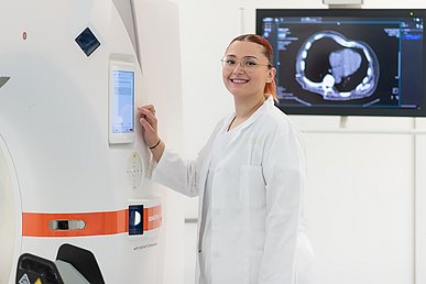 Mitarbeiterin in einem weißen Kittel nimmt über ein Display Einstellungen an einen CT-Gerät vor.