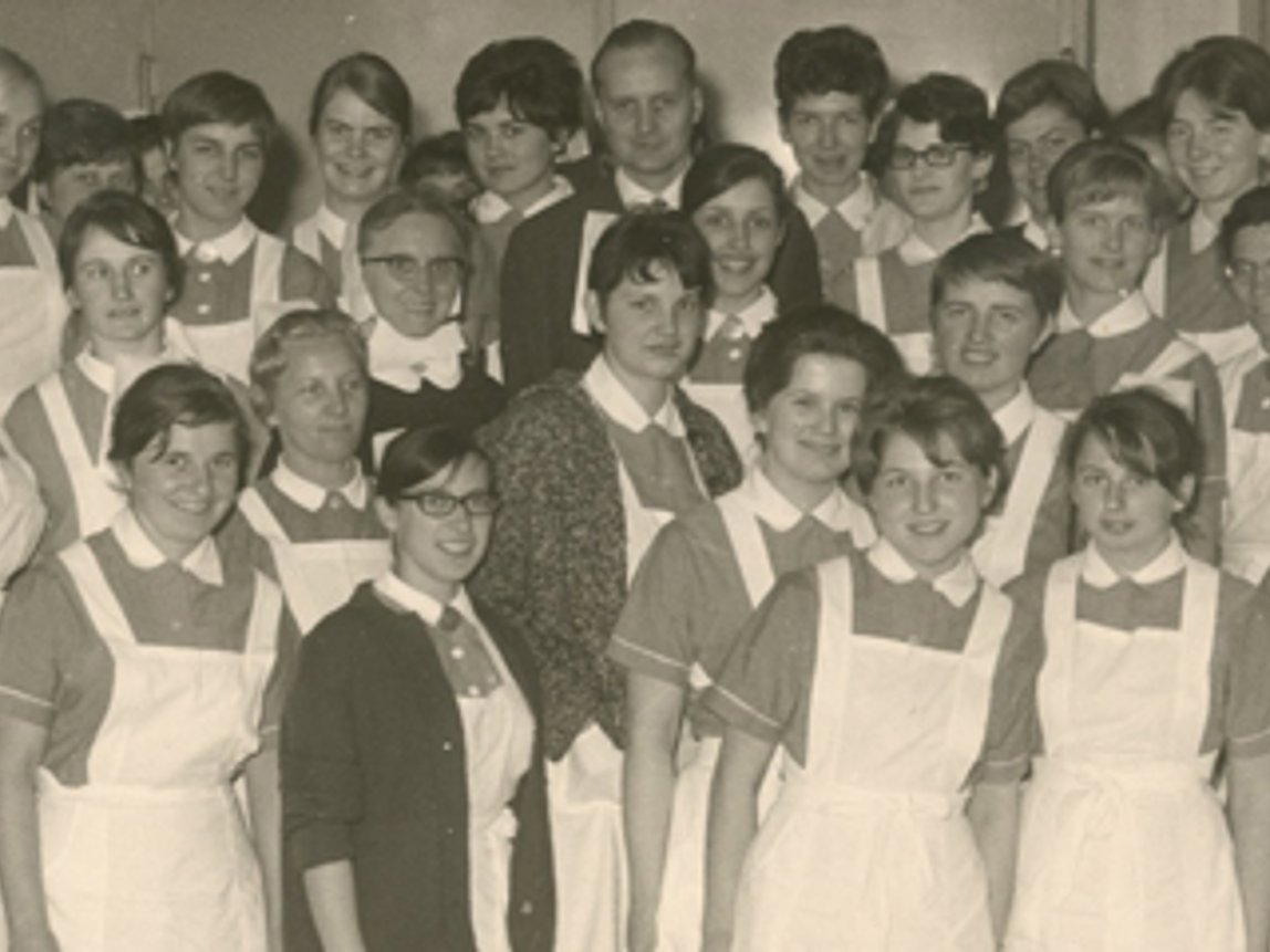 Altes Sepiafoto zeigt Mädchen mit Arbeitsuniform: Kurzarmblus und weißer Kittelschürze.