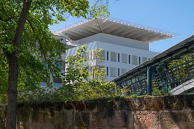 Hinter der grün bewachsenen historischen Stadtmauer aus Sandstein Sicht auf den weißen Neubau des Chirurgischen Zentrums. Auf dem Gebäude ein quadratischer Hubschrauberlandeplatz.