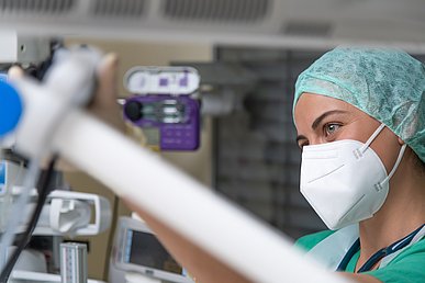 Seitliche Porträtaufnahme einer Mitarbeiterin  in einem Herzkatheterlabor mit OP-Kleidung und FFP2-Maske.