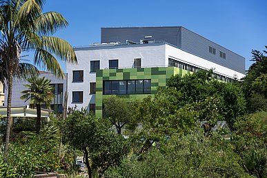 Moderner Anbau der Kinder- und Jugendklink vom Botanischen Garten aus aufgenommen. Die sich durchdringenden Kuben sind teils mit Metallplatten in verschiedenen Grüntönen verkleidet.