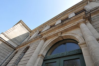 Blick von schräg unten auf ein historisches Sandsteingebäude mit Ziersäulen. Die Eingangstür aus grünem Holz mit halbkreisförmigen Oberlicht trägt in Jugendstil-Lettern die Beschriftung Pathologisches Institut