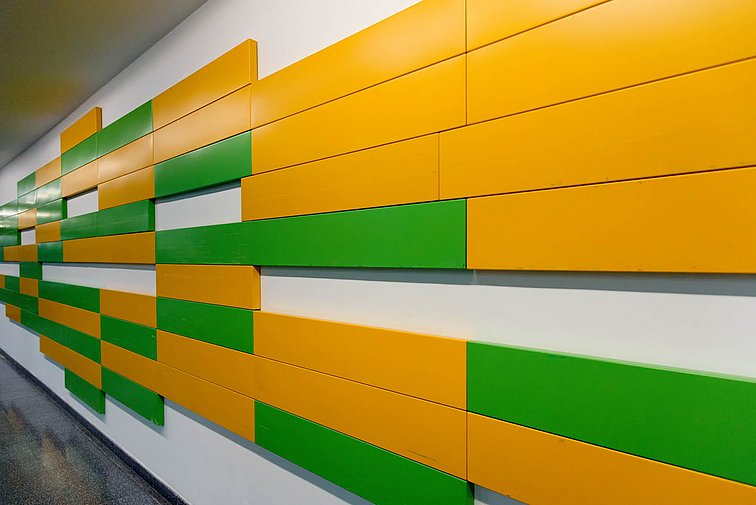 Das Werk hat die Form einer in die Breite gezogenen verpixelten grün-gelben Raute. Links sind mehr grüne Rechtecke, rechts mehr gelbe und in der Mitte eine Mischung aus beiden Farben.