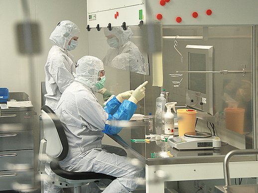 2 Fachkräfte in Ganzkörper-Schutzausrüstung mit Masken arbeiten in einem Abzug an Medikamenten.