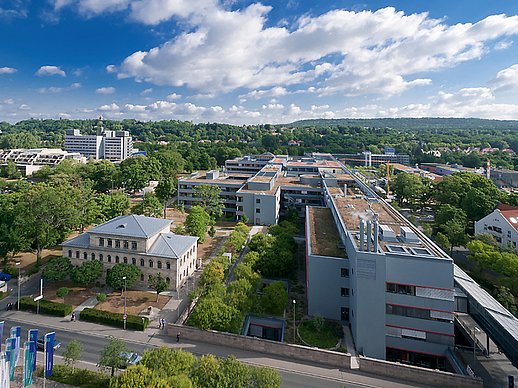 Blick aus der Luft auf das historische Gebäude der kaufmännischen Direktion links und rechts daneben das lang gestreckte internistische Zentrum umrahmt von Bäumen.